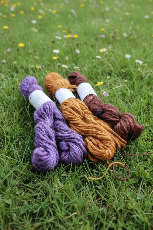 Three skeins of yarn in brown, orange, and purple on a textured surface.