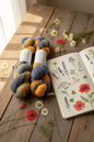 Baby alpaca silk yarn skeins on rustic table with sketchbook and wildflowers